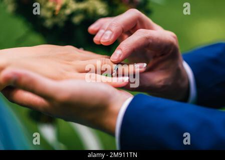 marié met la mariée un anneau de mariage d'or blanc sur son doigt. Gros plan sur les anneaux échangeant les mains lors de la cérémonie Banque D'Images