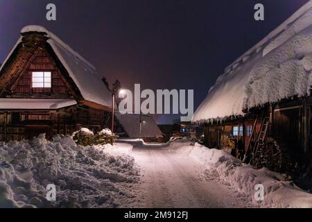 La neige s'accumule le long de la route dégagée par des maisons traditionnelles en bois dans le village la nuit Banque D'Images