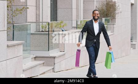 Bonne ethnie africaine l'homme d'affaires américain ethnique barbu marcher près de magasin de construction de centre commercial dans la ville à l'extérieur avec des achats. Souriant homme satisfait gars Banque D'Images