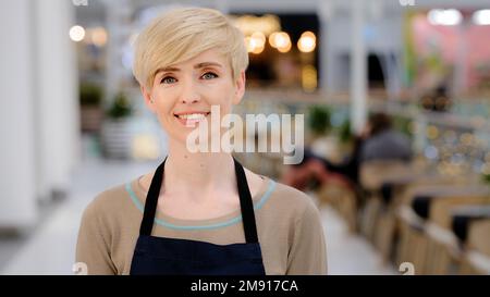 Gros plan femme Barista adulte. Portrait serveuse caucasienne femme d'âge moyen blonde avec une coupe courte sourire en dents de souris en regardant l'appareil photo sourire. Vue de dessus Banque D'Images