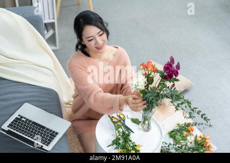 La jeune femme à la maison organisant des fleurs Banque D'Images