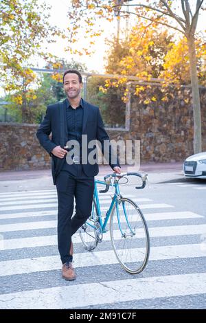 Un homme d'affaires afro-américain élégant en costume traversant la rue avec le vélo. Banque D'Images