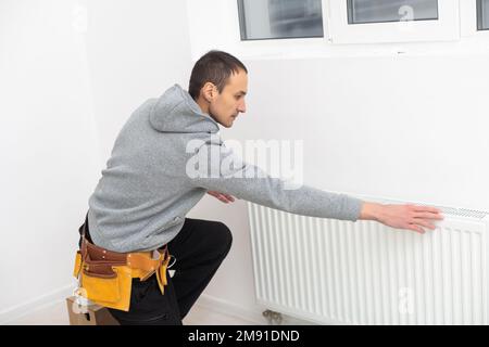 Un homme répare la batterie du radiateur dans la pièce. Travaux de réparation d'entretien rénovation de l'appartement. Restauration du chauffage Banque D'Images