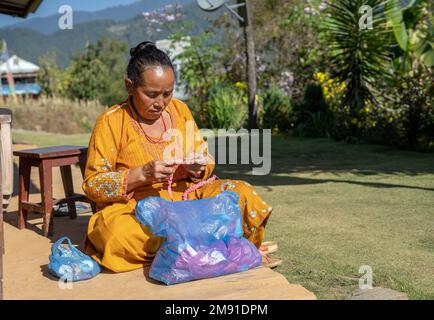 District de Dolakha, Népal - décembre 2022 - femme sénior à la maison dans l'arrière-cour nouant la laine ornement Banque D'Images