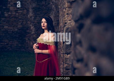 Une femme caucasienne avec une épée portant une robe rouge médiévale par une ancienne fortification Banque D'Images