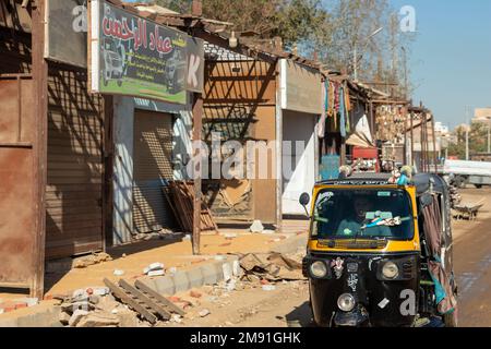 ASSOUAN, ÉGYPTE - 28 décembre 2022. Les gens locaux dans les transports traditionnels tuc tuc avec des magasins fermés dans les rues d'Assouan, Afrique Banque D'Images