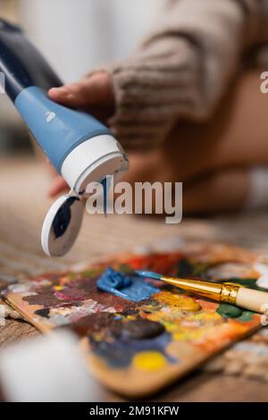 Vue rognée de l'artiste versant de la peinture sur la palette près du pinceau dans l'atelier Banque D'Images