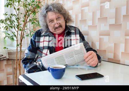Un portrait d'un pensionné âgé lisant un journal à la maison avec une tasse de café Banque D'Images