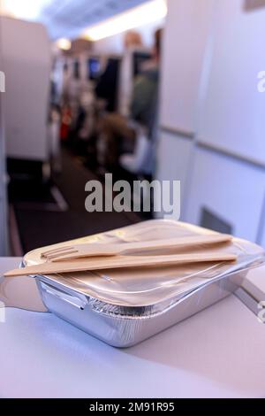 Repas chaud dans une boîte en aluminium avec des couverts en bois sur la table d'un passager dans un avion volant Banque D'Images