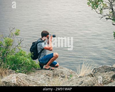 photographe touriste mâle prenant des photos assis sur le bord d'une falaise paysage Banque D'Images