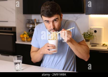 Un adorable gars mangeant des nouilles instantanées dans la cuisine Banque D'Images