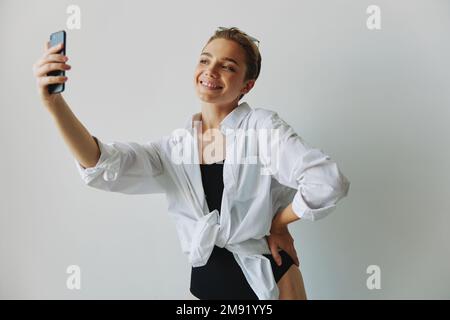 Une jeune fille blogger prend des photos et des pousses. elle-même sur la vidéo sur son téléphone pour le contenu de médias sociaux, blogueur vidéo, se selfie contre un mur blanc avec Banque D'Images