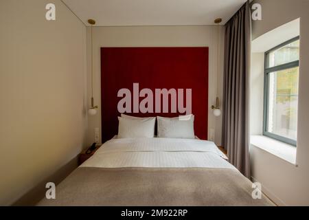 oreillers blancs sur un lit moderne près du mur rouge dans la chambre d'hôtel, image de stock Banque D'Images