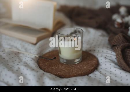 Décoration intérieure douillette avec un livre, une bougie et une branche de coton dans un lit doux et chaleureux. Maison agréable Banque D'Images