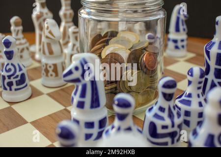 pièces en euros dans un pot en verre sur l'échiquier parmi les pièces d'échecs Banque D'Images