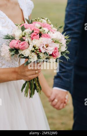 Le bouquet de mariage de la mariée de fleurs roses fraîches dans sa main et tenant les mains avec le marié. Détails du mariage. Banque D'Images