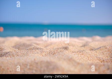 Gros plan sur une surface de sable jaune propre couvrant la plage de bord de mer avec de l'eau de mer bleue sur fond. Concept de voyage et de vacances Banque D'Images