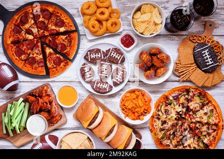 Scène de table de nourriture sur le thème du Super Bowl ou du football. Pizza, hamburgers, ailes, encas et accompagnements. Vue ci-dessus sur un fond en bois blanc. Banque D'Images