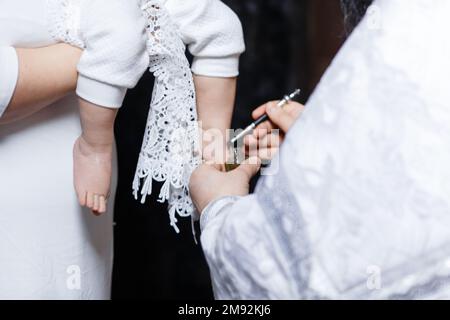 Jeunes parents à l'église avec leur bébé portant une robe de baptême . Photo de haute qualité Banque D'Images