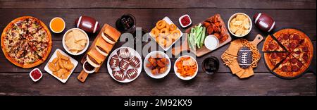 Scène de table de nourriture sur le thème du Superbowl ou du football. Pizza, hamburgers, ailes, encas et accompagnements. Vue ci-dessus sur un arrière-plan de bannière en bois sombre. Banque D'Images