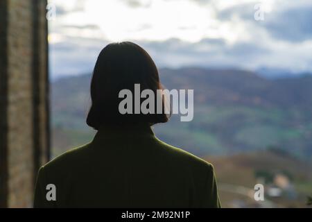 Vue arrière de jeunes femmes attentionnée avec de courts cheveux bruns ondulés debout contre le paysage flou pendant la journée d'automne à Santa Vittoria à Matenano Banque D'Images