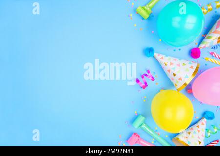 Bordure latérale de fête d'anniversaire sur fond bleu. Vue ci-dessus avec confettis, ballons, chapeaux de fête et banderoles. Copier l'espace. Banque D'Images