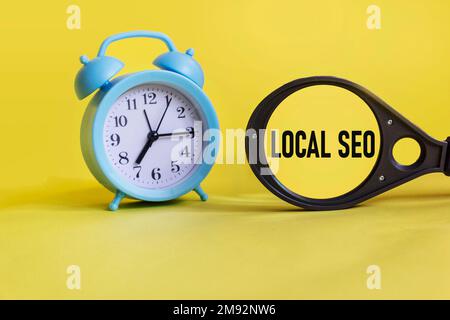 SEO local écrit sur une loupe, sur un fond jaune avec une horloge Banque D'Images