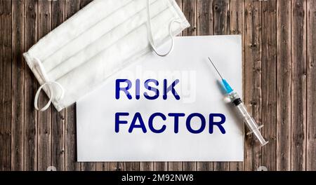 Sur un fond en bois, une seringue, un masque médical et une feuille de papier avec le facteur DE RISQUE de texte à l'intérieur. Vue de dessus. concept médical Banque D'Images