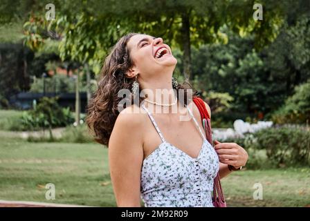 Bonne jeune femme en robe d'été riant tout en appréciant la journée ensoleillée dans le parc Banque D'Images