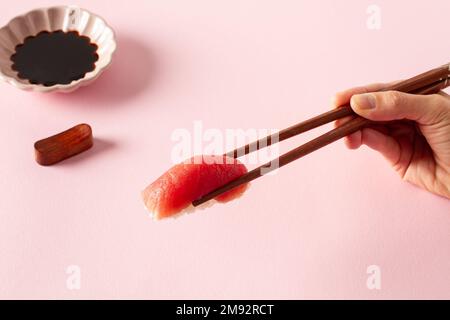 Du dessus de la récolte anonyme à la main prenant délicieux sushi avec des baguettes sur table rose près de la sauce de soja Banque D'Images