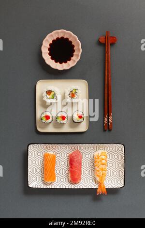 Plat de divers petits pains à sushis placés sur des assiettes avec des baguettes et de la sauce soja sur fond gris Banque D'Images