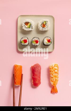 Plat de divers petits pains à sushis placés sur des assiettes avec des baguettes et de la sauce soja sur fond rose Banque D'Images