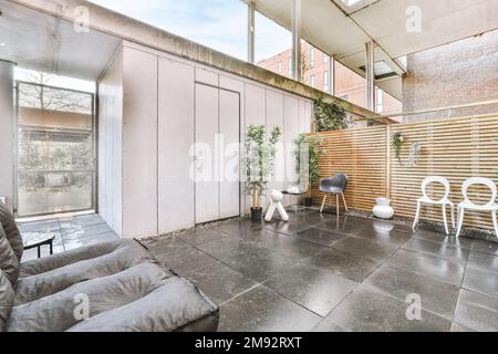 Sièges confortables et plantes en pot situées sur le sol carrelé dans le couloir de l'immeuble contemporain en journée Banque D'Images
