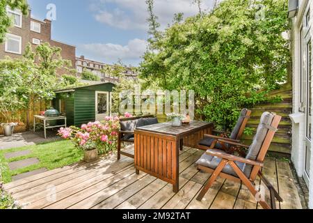 Table avec chaises sur la terrasse en bois située près des buissons verts et pelouse dans la cour contre le ciel bleu dans la banlieue Banque D'Images