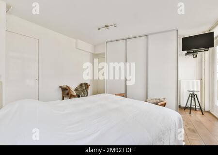 Décoration intérieure de chambre minimaliste contemporaine avec murs blancs, grand lit contre armoire et TV Banque D'Images