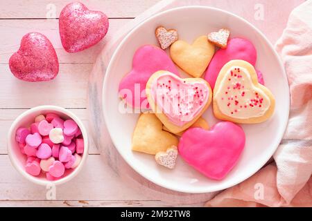 Biscuits de Saint-Valentin en forme de coeur avec glaçage rose et blanc et saupoudrage. Vue de dessus scène de table sur fond de bois blanc. Banque D'Images