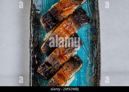 Nigiri à l'anguille fumée grillée sur une assiette en céramique bleue Banque D'Images