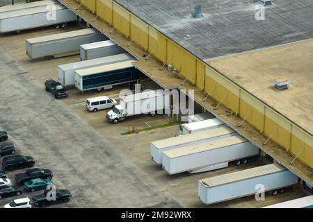 Vue de dessus du centre logistique géant avec de nombreux camions de remorques commerciales qui déchargent et chargent des produits de vente au détail pour une expédition ultérieure. Économie mondiale Banque D'Images