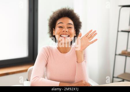 Gaie jeune femme de course mixte agitant la main, parlant, tournage vlog, a appel vidéo à table Banque D'Images