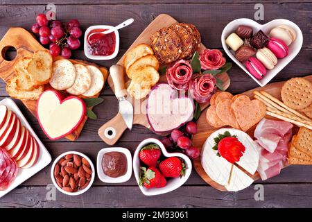 Table charcuterie sur le thème de la Saint-Valentin sur fond de bois sombre. Assortiment de fromages, viande, fruits et hors-d'œuvre sucrés. Vue de dessus vers le bas. Banque D'Images