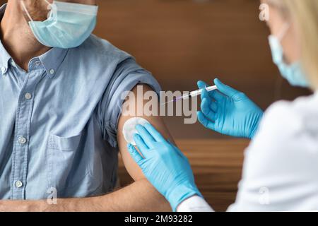 Une infirmière féminine effectue une injection de vaccin chez un jeune homme Banque D'Images