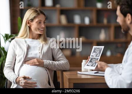 Gynécologue Docteur montrant l'image d'échographie de bébé à la jeune femme enceinte en clinique Banque D'Images
