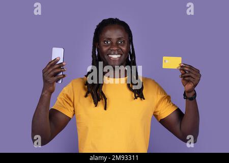 Homme noir souriant tenant un smartphone et une carte de crédit Banque D'Images