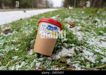 Hiver. Une tasse de café avec un autocollant patriotique se trouve sur la pelouse (gros plan). Traduction de l'inscription sur l'autocollant - tout sera Ukraine Banque D'Images