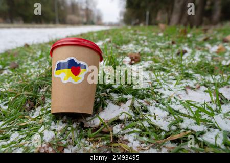 Hiver. Le sol est recouvert d'une petite couche de neige. Une tasse de café avec un autocollant patriotique « I love Ukraine » se trouve sur la pelouse (gros plan) Banque D'Images