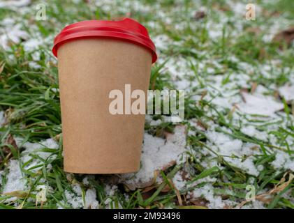 Hiver. Temps froid. Le sol est recouvert d'une petite couche de neige. Une tasse de café repose sur la pelouse (gros plan) Banque D'Images