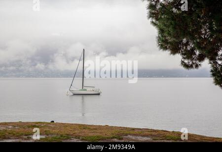Ambiance de nature et voilier abrité dans l'eau d'hiver et vue à travers les arbres sur le lac de Lugano avec brouillard. Hiver décembre sur le lac majeur Banque D'Images