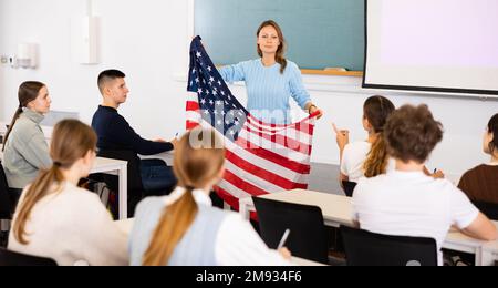 Leçon de géographie en classe scolaire - un professeur parle des Etats-Unis d'Amérique, en tenant le drapeau entre ses mains Banque D'Images