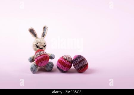 Trois oeufs décoratifs de Pâques tricotés dans les tons lilas et pourpres et lapin gris tricoté sur un fond violet. Concept joyeuses Pâques. Carte de vœux avec Banque D'Images