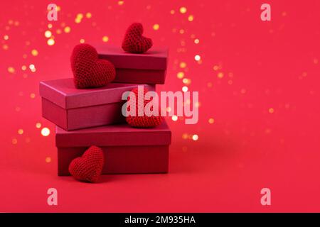 Trois boîtes-cadeaux rouges avec coeurs rouges crochetés sur fond rouge et lumières de fête dorées. Bonne Saint Valentin, fête des mères et anniversaire Banque D'Images